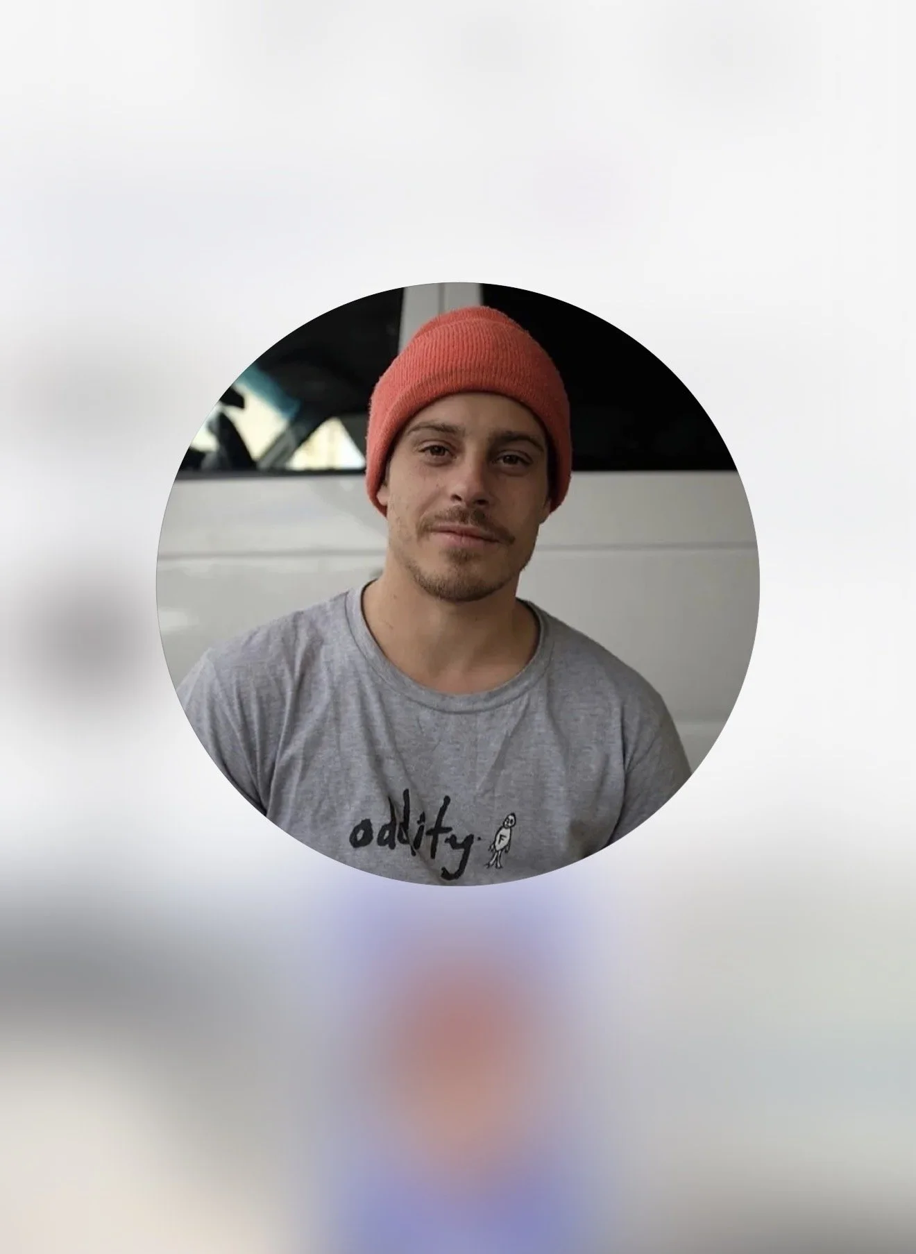 A young man wearing a red beanie and a gray t-shirt with a graphic and the word 'addity' printed on it, standing outside near a white vehicle.