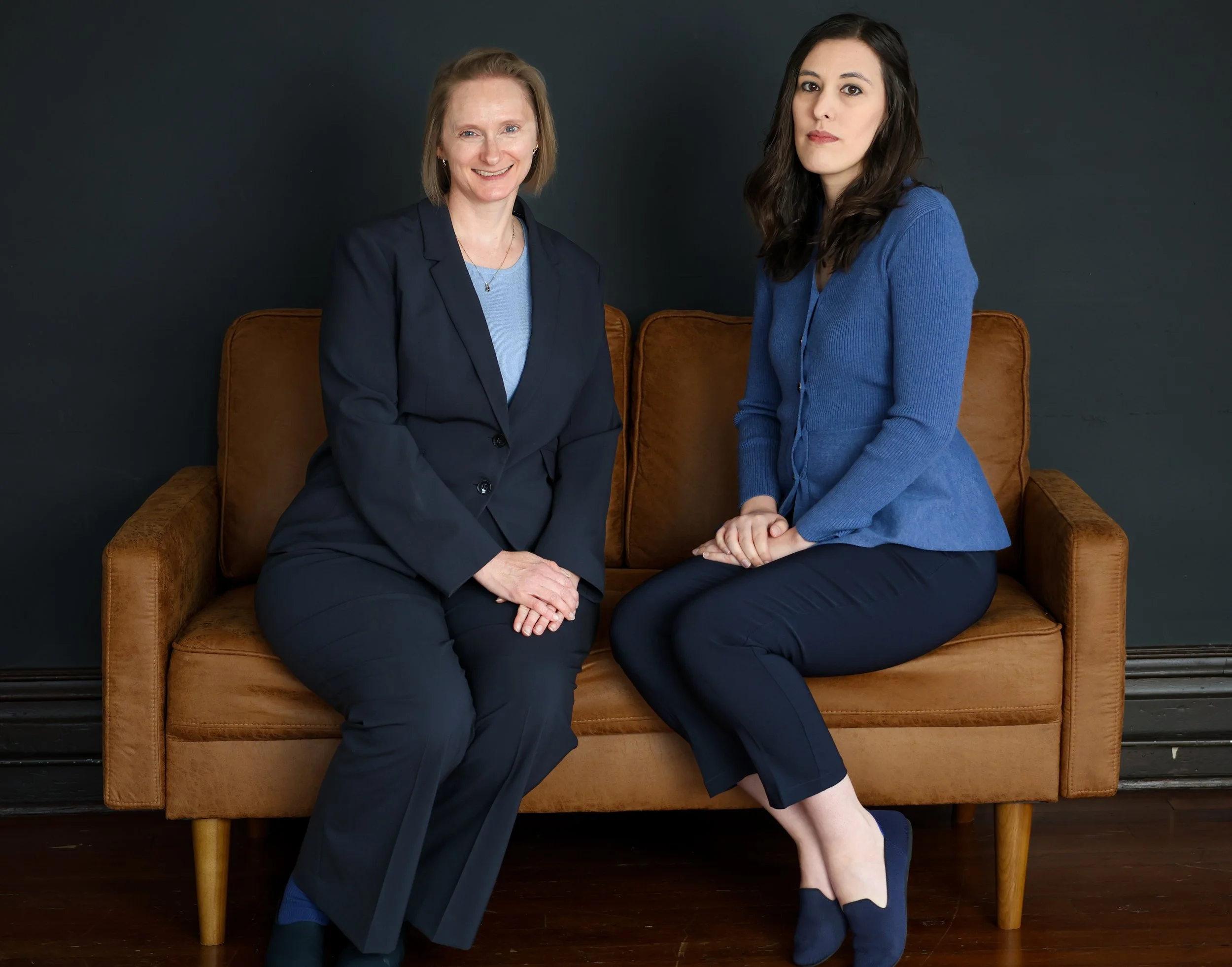 Tyrie and Patty portrait, sitting on a brown leather couch with a dark background
