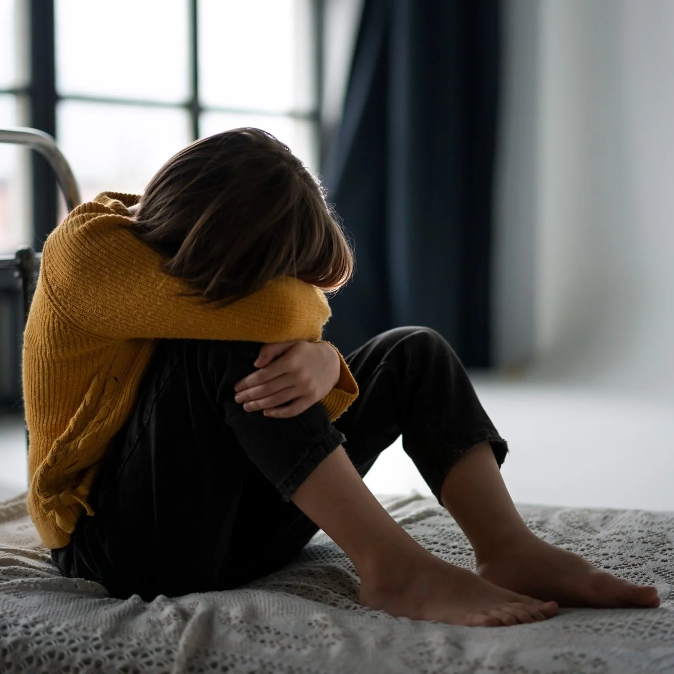 Child sitting alone with head resting on knees, representing family stress, fear, or child protection concerns.