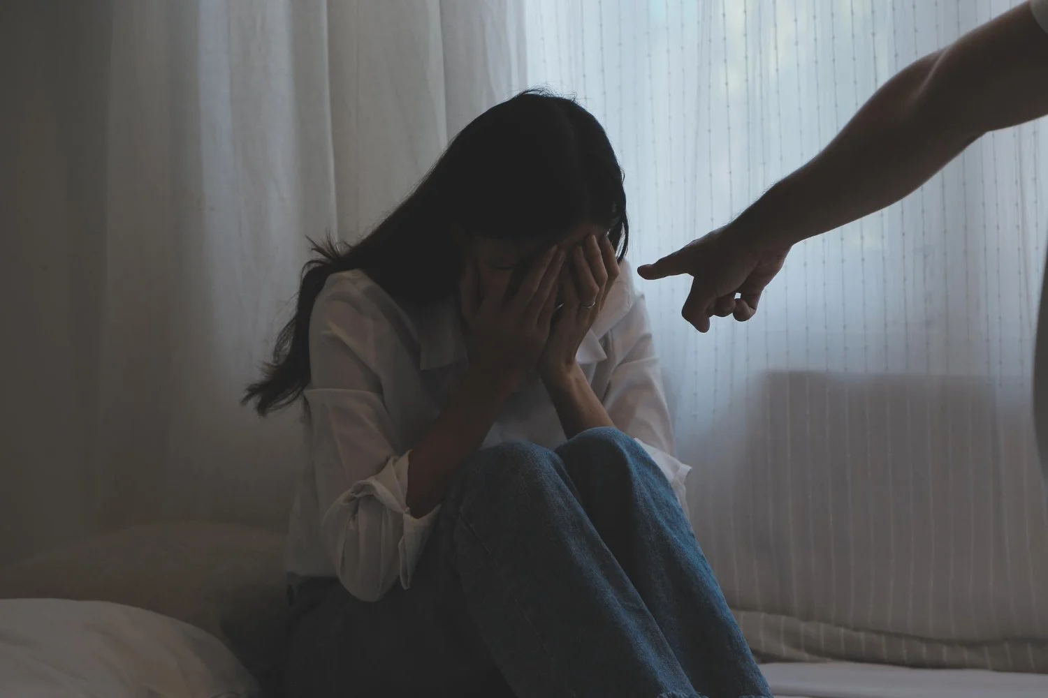 Person covering their face while another person points at them, representing fear, intimidation, or emotional abuse.