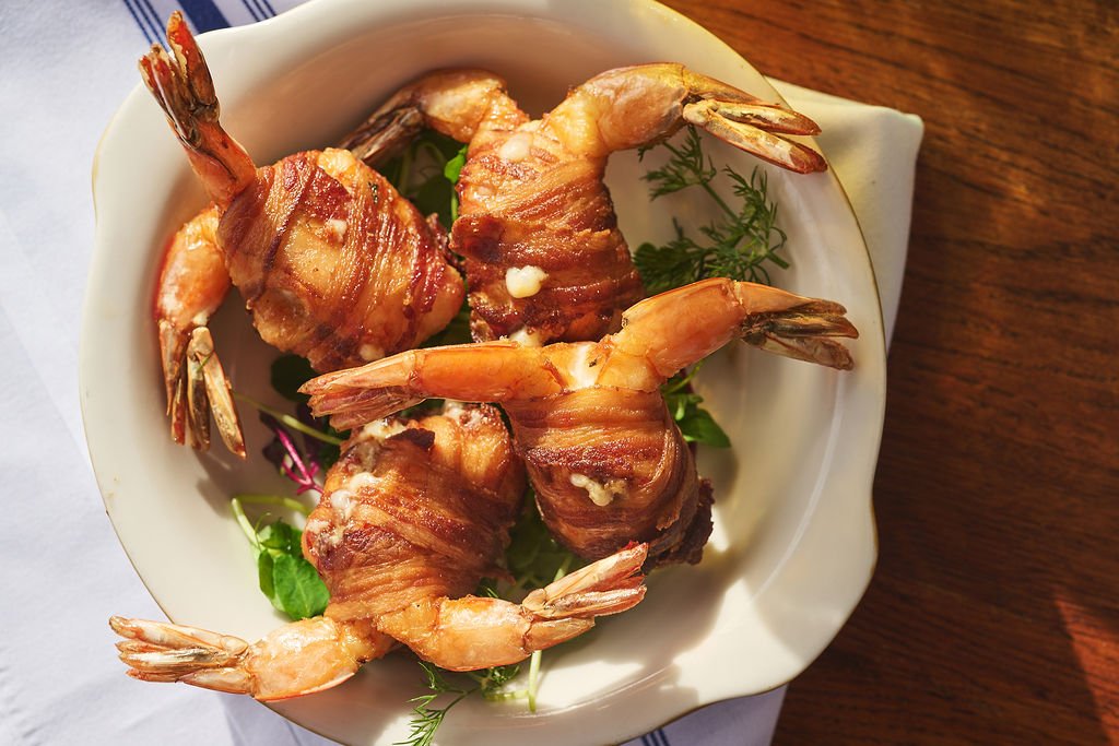 Bacon-wrapped shrimp on a bed of greens in a white bowl
