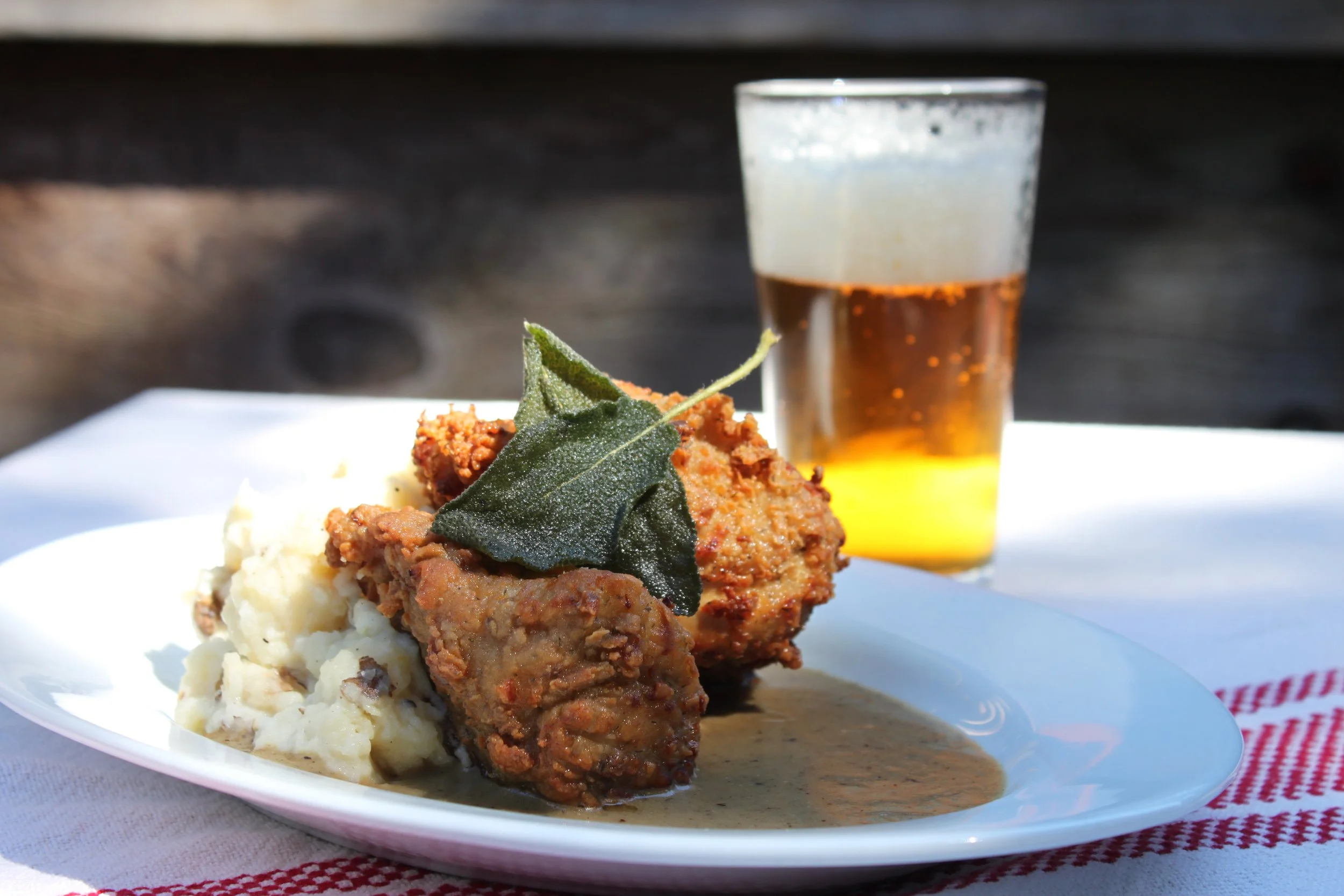 Plate of mashed potatoes and fried chicken with a green leaf garnish, accompanied by a beer in the background.