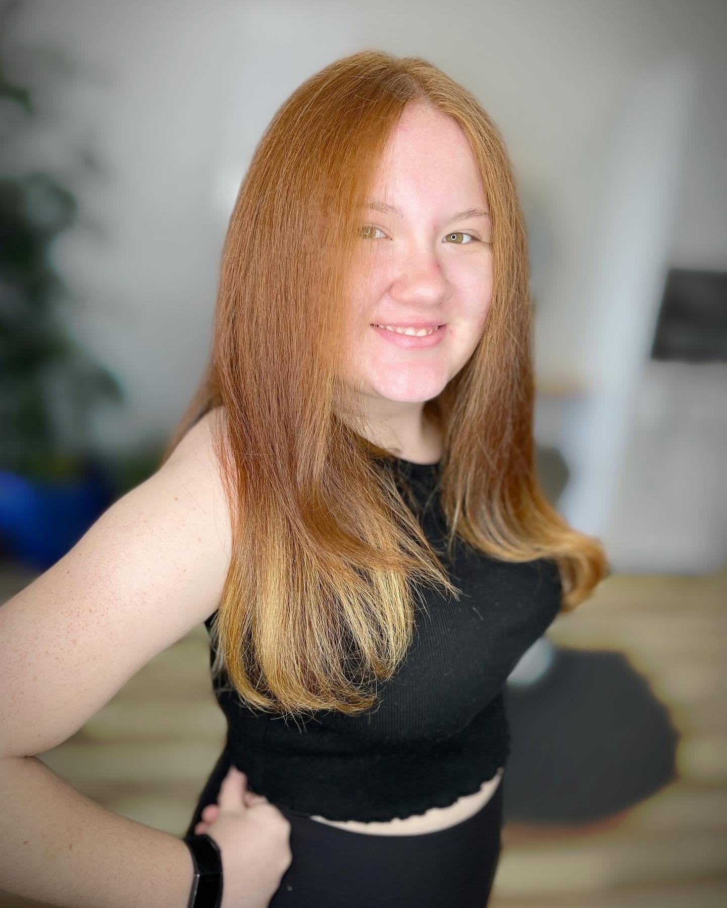 Young woman with long, red hair taking a selfie in a room with a blurred background.