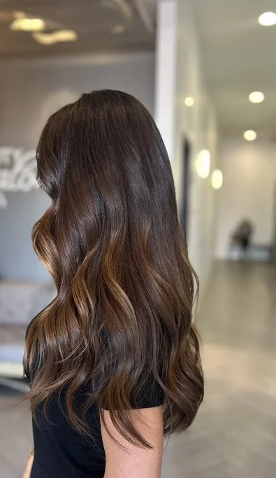 Side view of a woman with long, wavy, brown hair in a modern indoor setting.