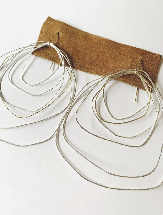 Rara Avis Objects Jewelry - A pair of large gold hoop earrings with multiple concentric hoops hanging from hooks, attached to a brown leather strip.