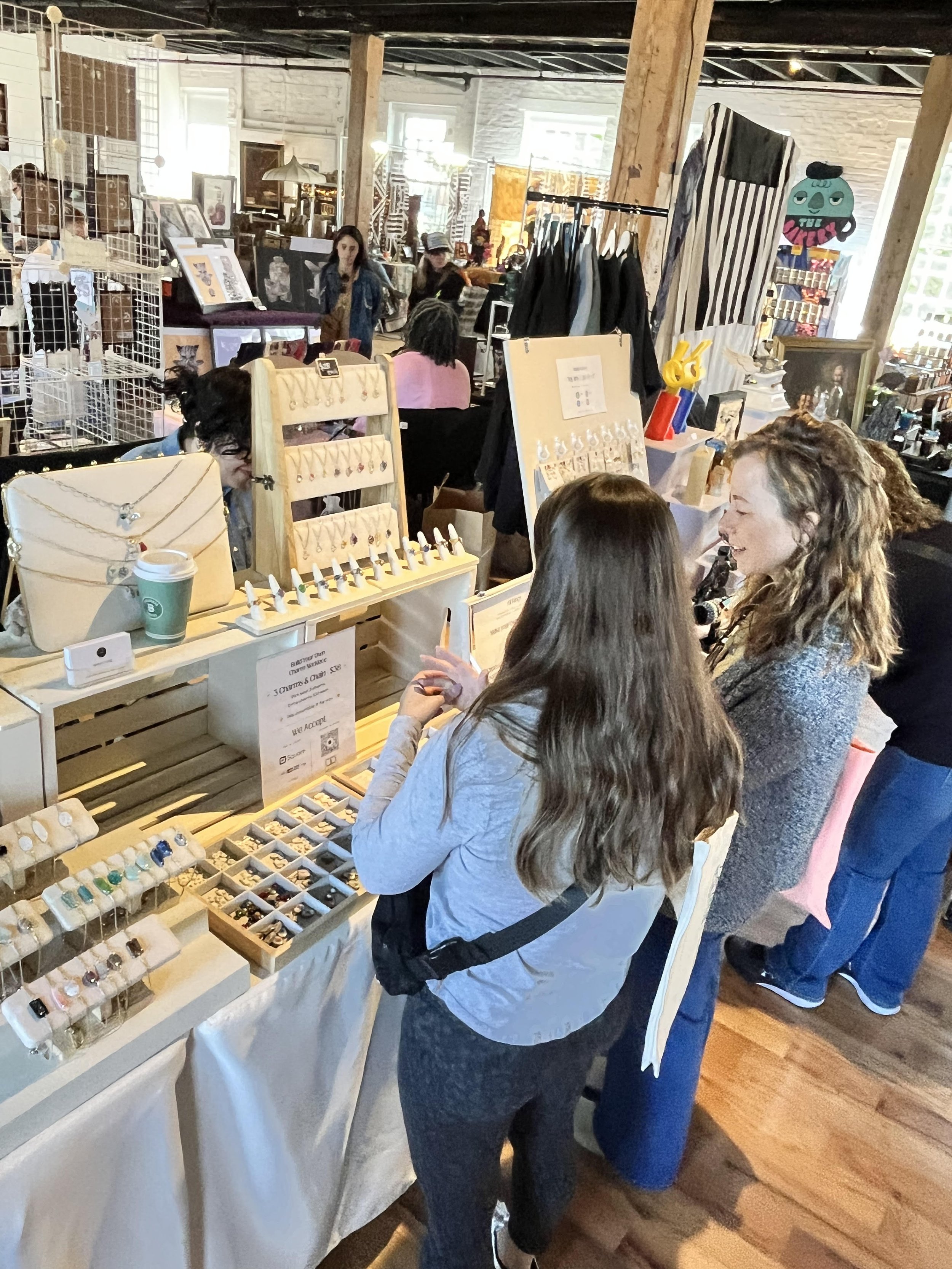 People browsing jewelry at a marketplace stall that displays rings, necklaces, and earrings.