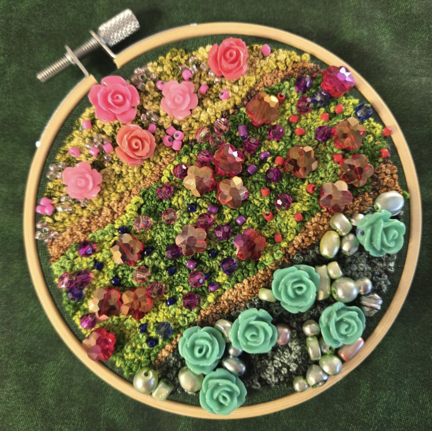 Embroidered Moose - A circular embroidery hoop filled with colorful embroidery stitches and decorated with pink roses, beads, and sequins on a green fabric background.