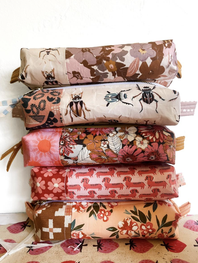 Six colorful fabric pencil cases stacked vertically, featuring floral, bee, animal, and geometric patterns.