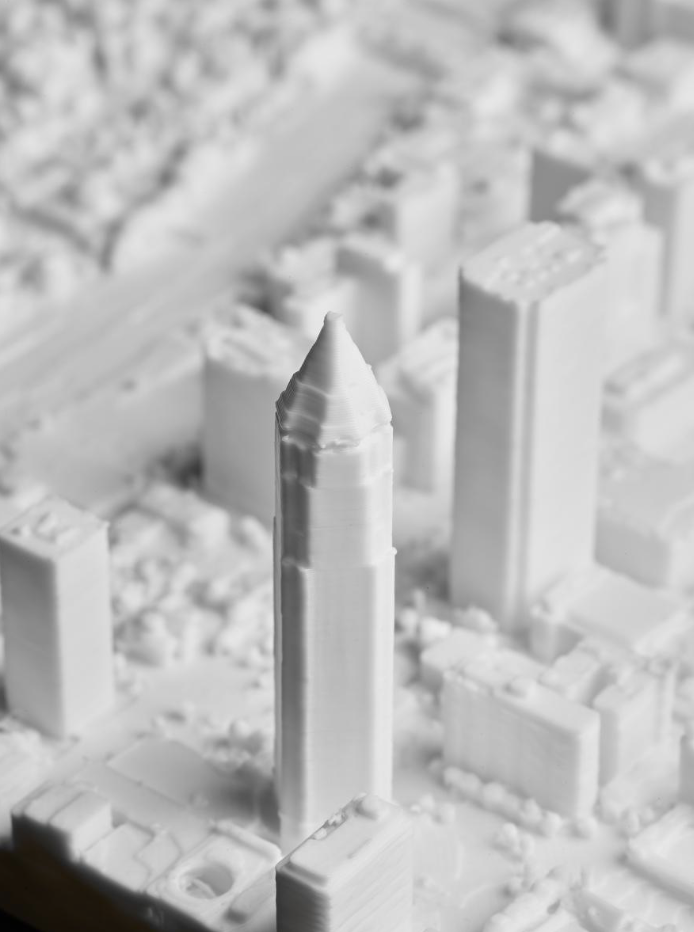 Peak Prints - A white, 3D-printed model of a cityscape with a tall, pointed skyscraper in the center.