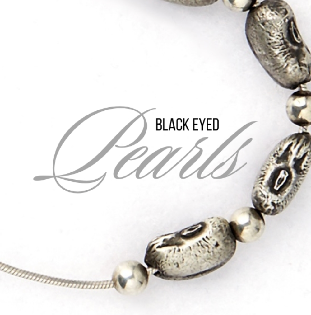 Black Eyed Pearls - Close-up of a silver necklace with pearl-like beads and black-eyed pearls, beside a card that reads "Black Eyed Pearls" in elegant font.