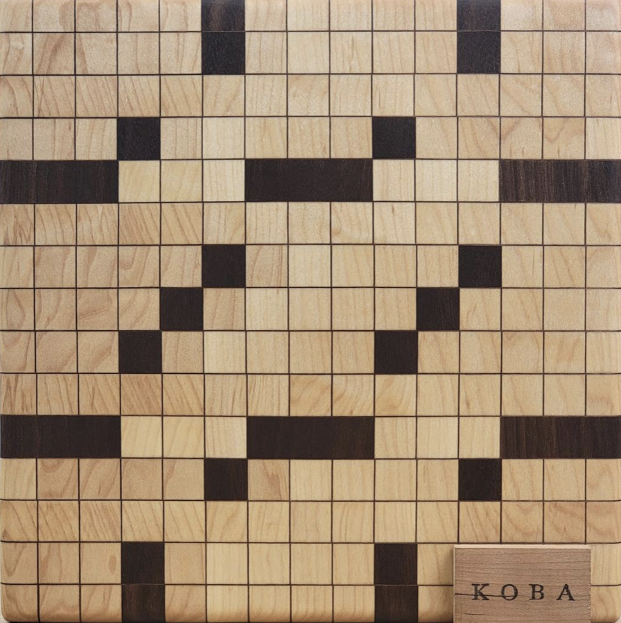 A wooden Kubb game board with a pixelated face design formed by darker wood squares, and a small wooden plaque with the word KOBA Wood Crafters
