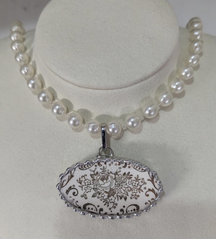 Little Sunshine Still - A pearl necklace with a large oval pendant featuring a floral pattern.