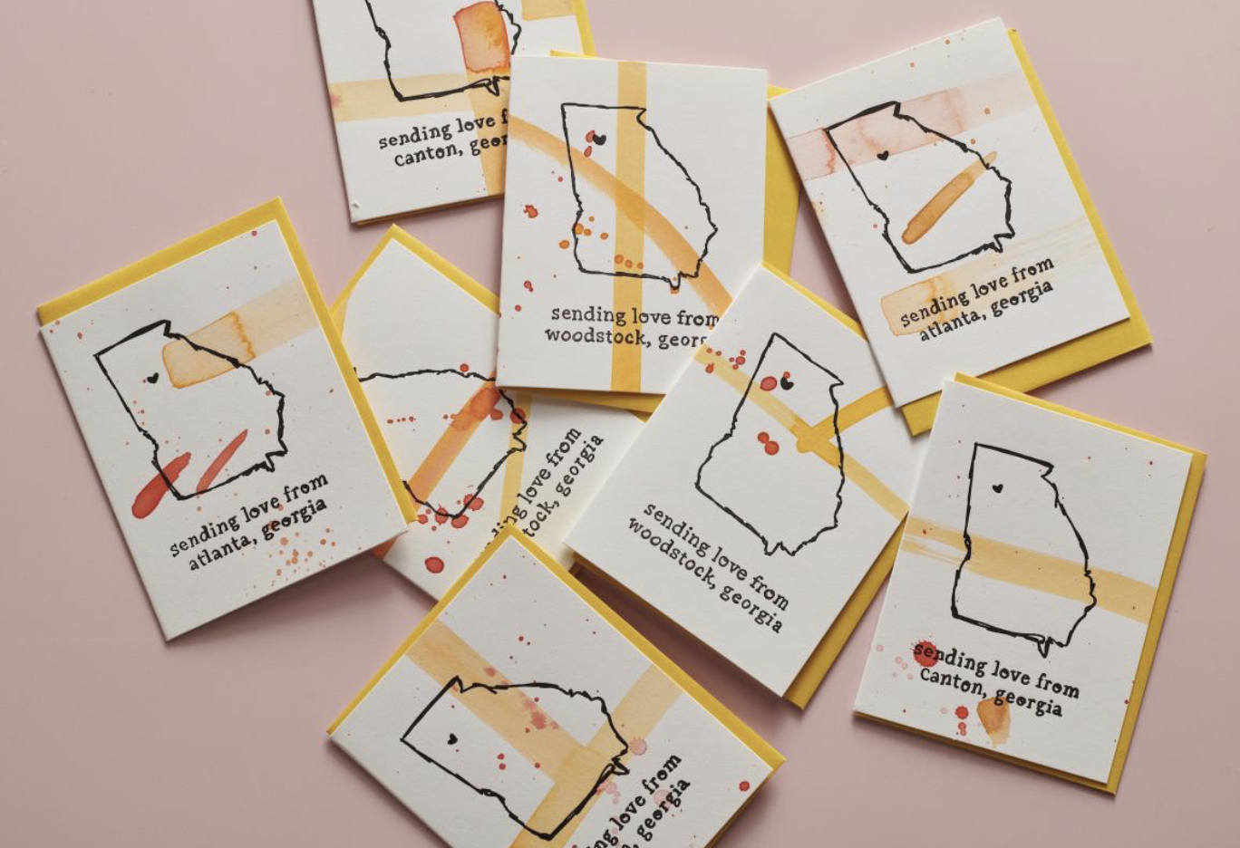 Beau Paper Co - Multiple handmade cards with Georgia state outline, watercolor splashes, and the text 'sending love from [city], Georgia' on a pink background.