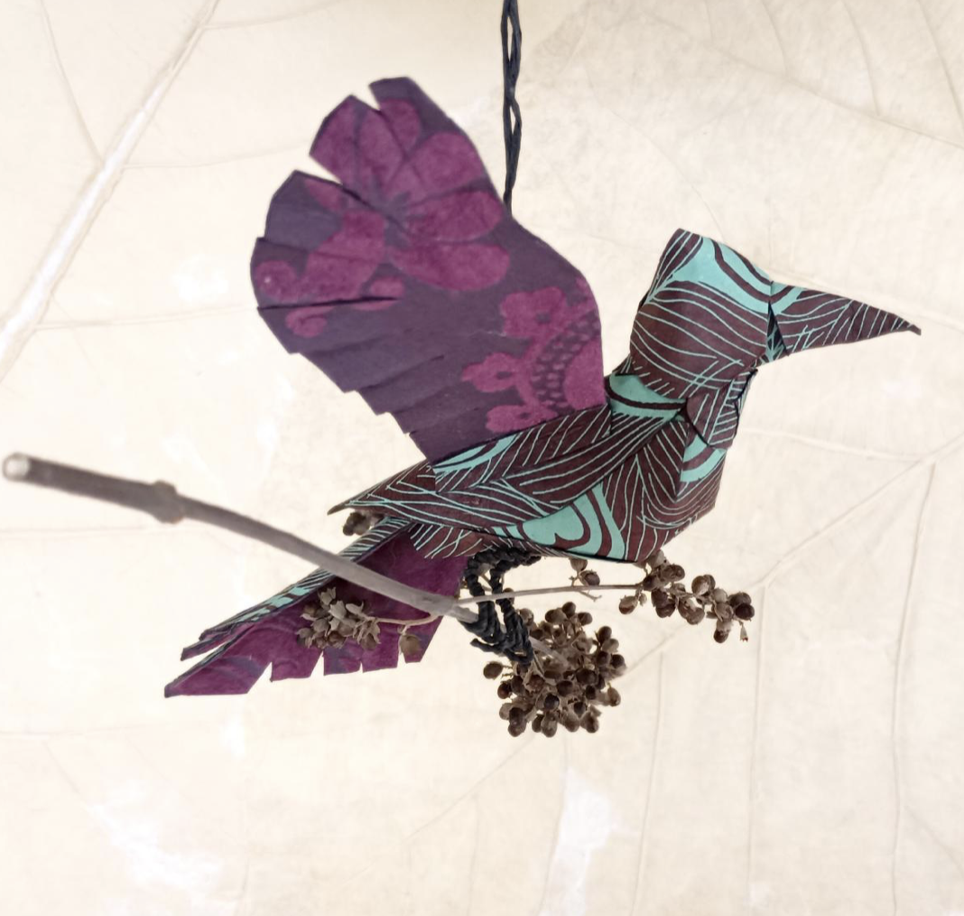 Flight Patterns - Origami owl and flowers hanging from a string, on a tiled surface.