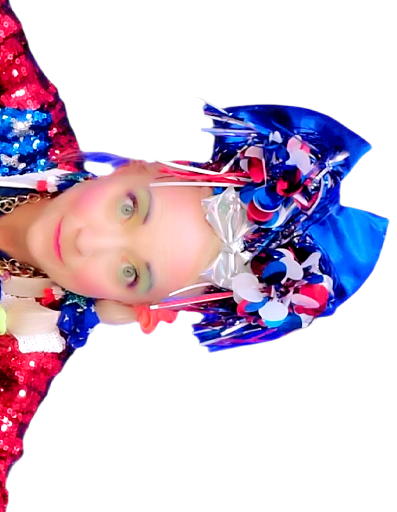Person wearing a patriotic-themed hat made of blue, white, and red ribbons and confetti, with preppy makeup and a red, white, and blue sequined top.