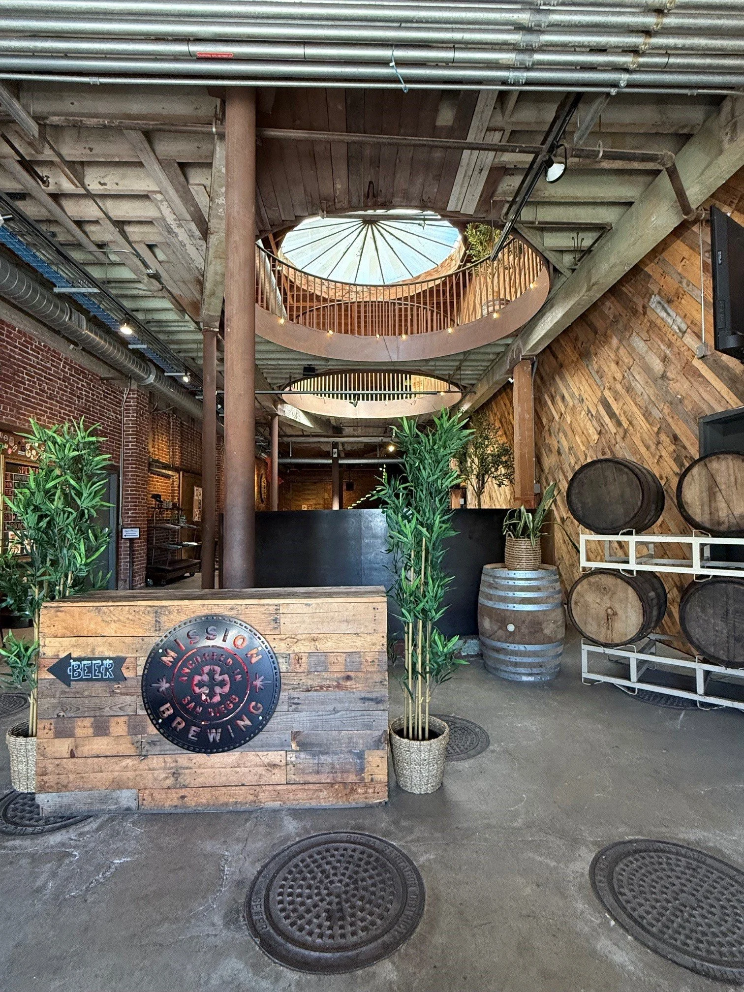 Indoor area of a brewery or pub with wooden decor, green potted plants, a liquor display, and a sign pointing to the beer selection.
