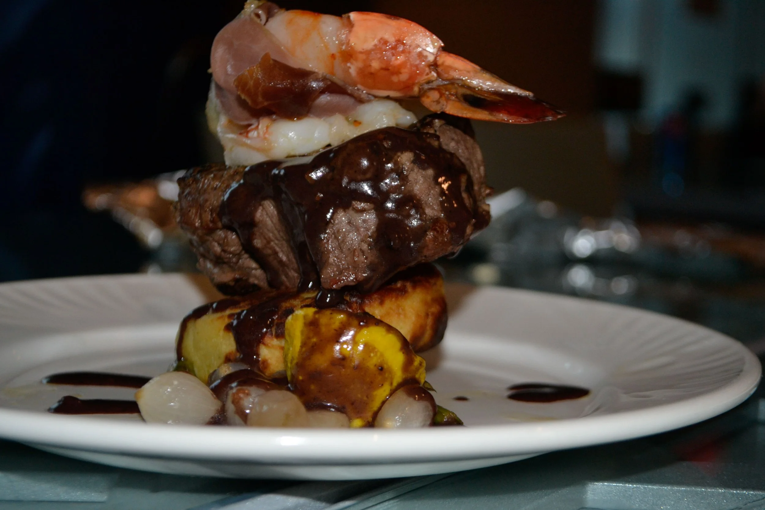 A dessert of skewered grilled fruit, cake, and meat, topped with chocolate sauce, served on a white plate.
