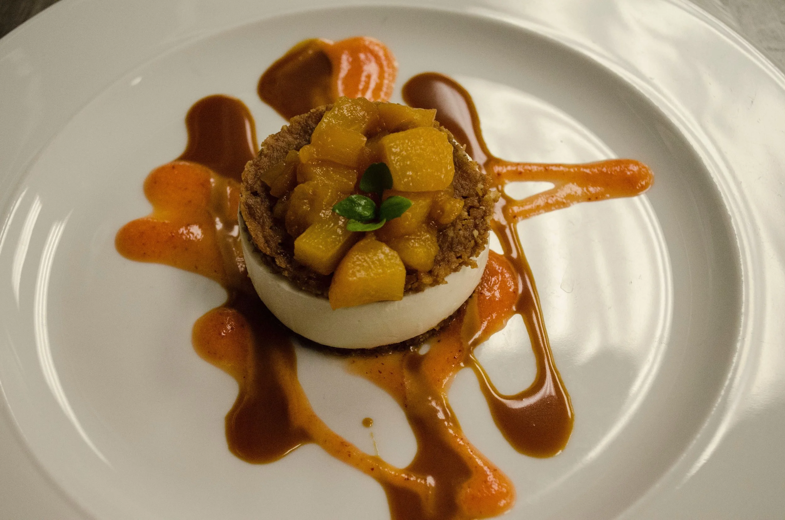 A plated gourmet appetizer consisting of a halved soft-boiled egg topped with a relish of diced yellow vegetables, garnished with a tiny fresh green herb, and drizzled with orange and brown sauces on a white plate.