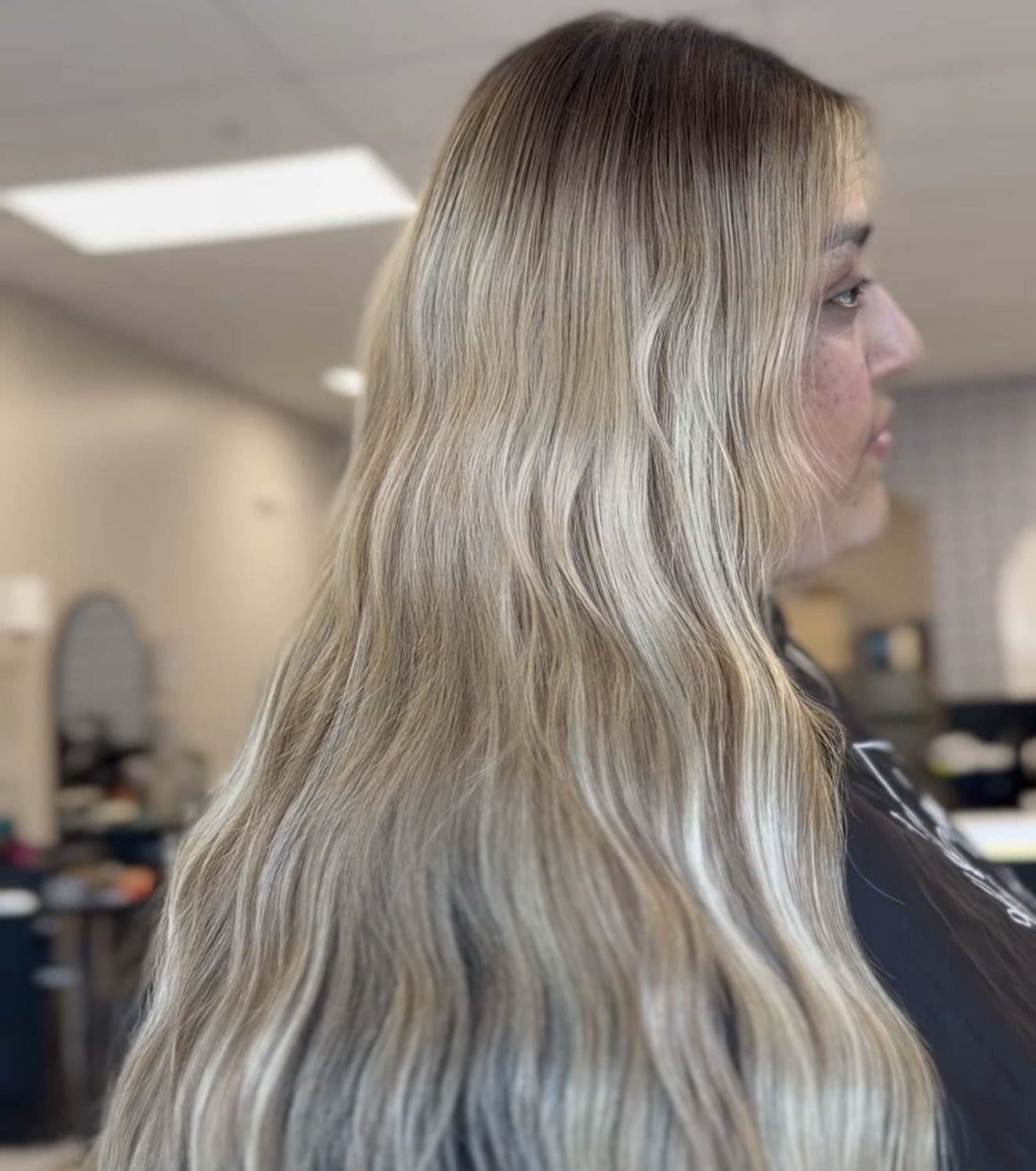 Side view of a woman with long, wavy, blonde hair in a salon or studio setting.