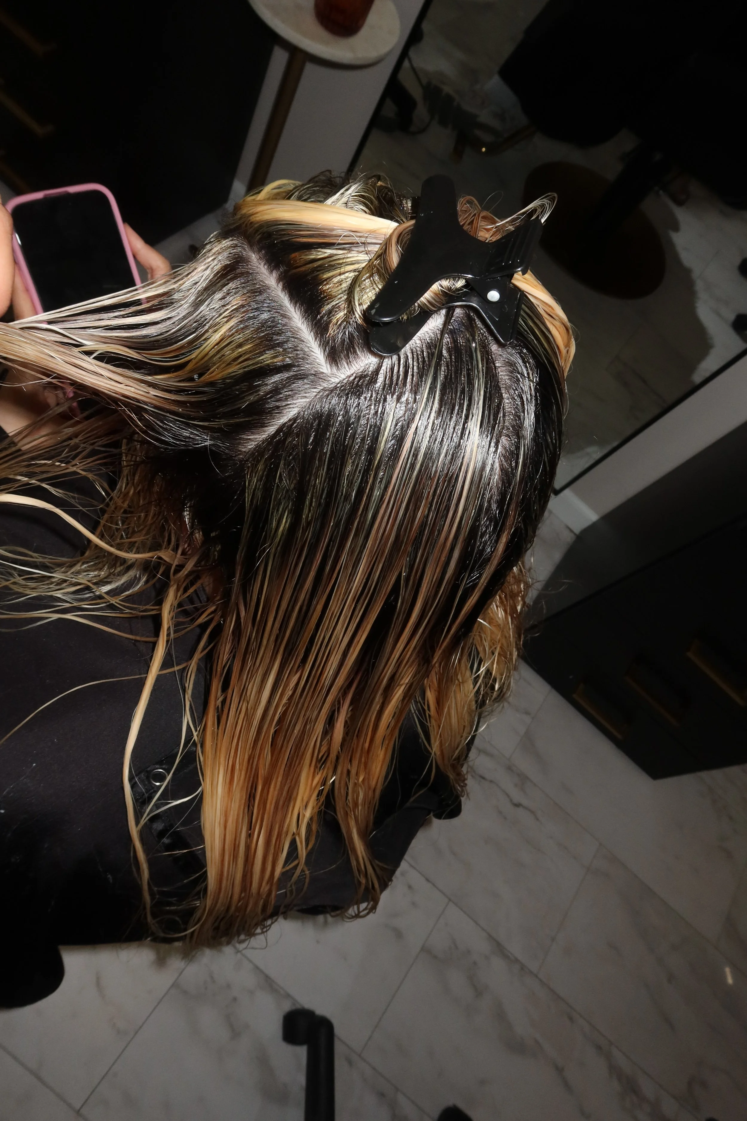 Person getting their hair dyed blonde at a salon, with foils in their wet hair and a hair clip in their hair.