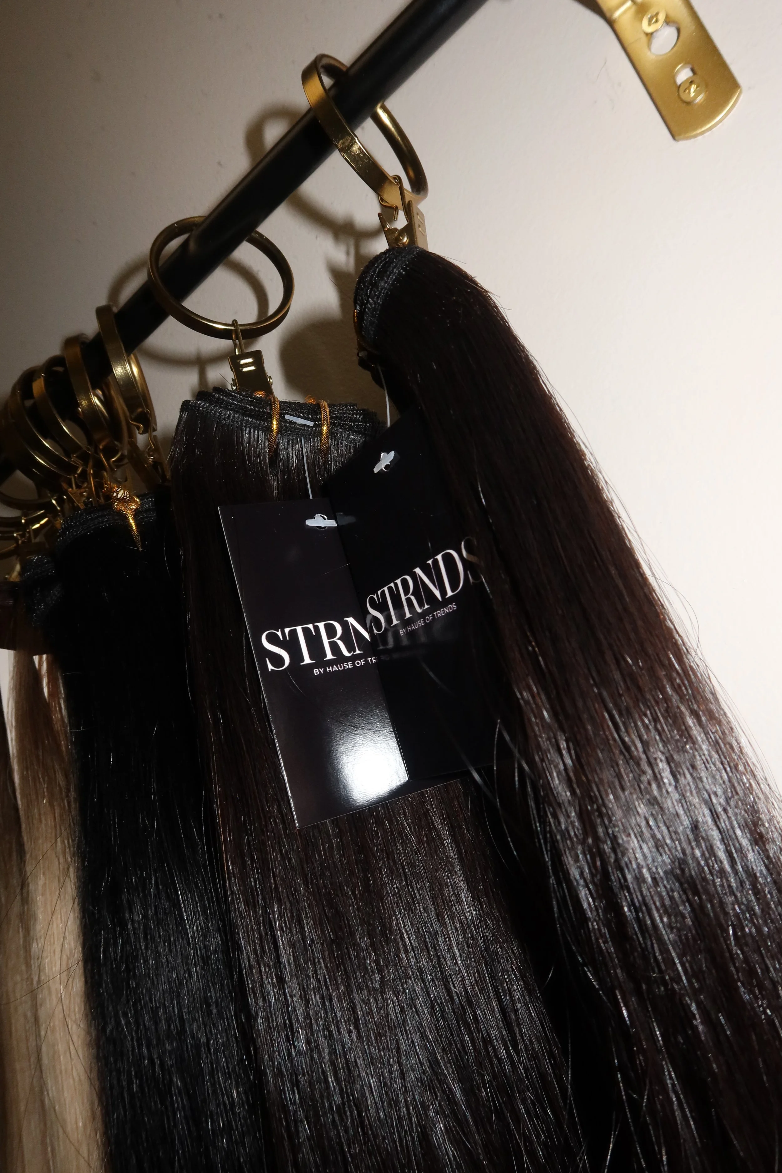Bundles of long, straight, dark brown hair extensions hanging from gold hooks on a black rod.