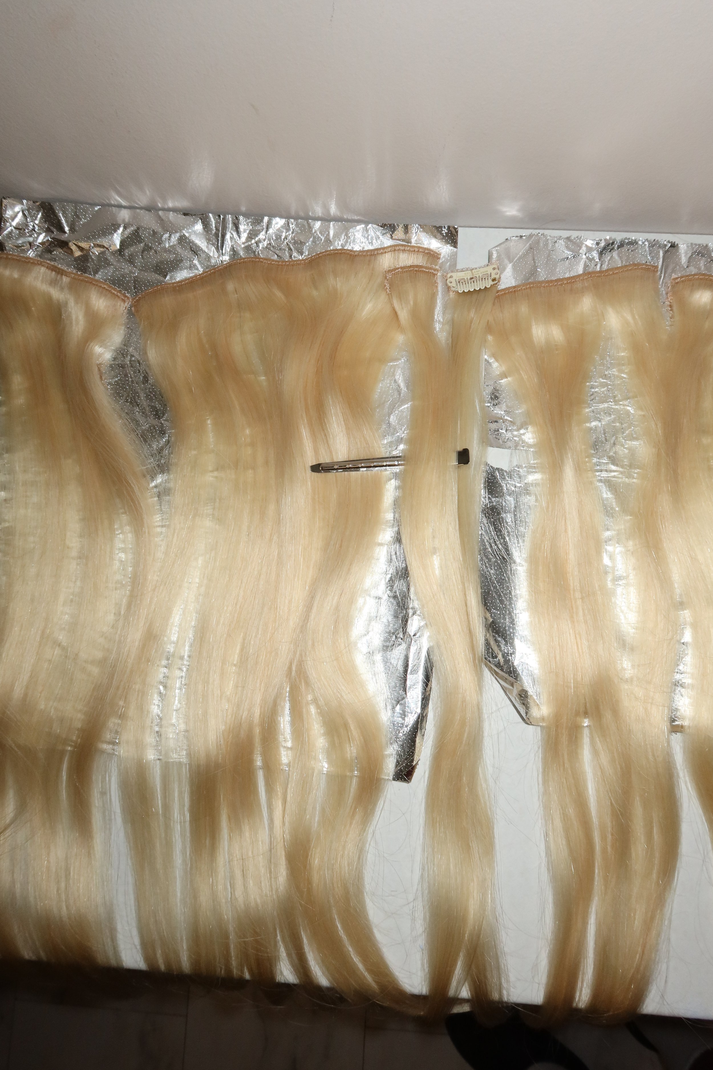 Blonde hair extensions in transparent plastic packaging on a white surface.
