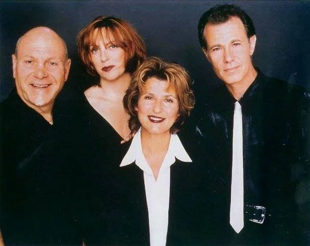 Four people posing for a portrait against a dark background, with two men and two women, all dressed in dark clothing.