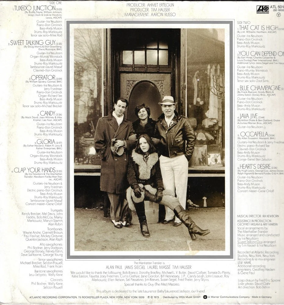 A black-and-white photo of four people posing together outside a building near a window with candles and other objects. The group includes two men and two women, with one woman sitting with her legs crossed. They are dressed in attire typical of the 