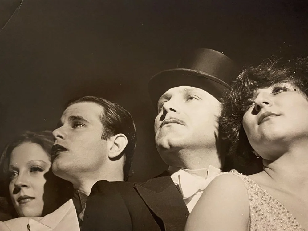 Black and white photo of four well-dressed people looking upward, possibly performers or actors in costume.