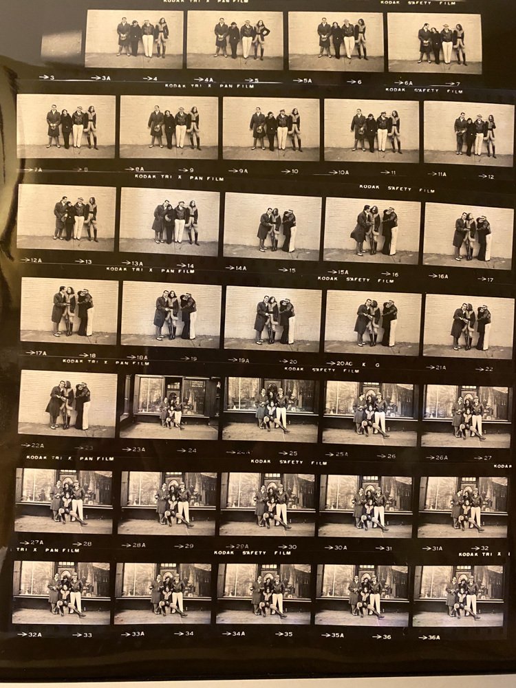 Strip of black-and-white contact sheet with multiple small photos of people posing outdoors and in front of a building, labeled with film processing info.