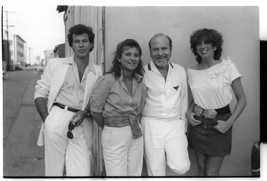 Five people standing outdoors on a street, smiling at the camera, black and white photo.