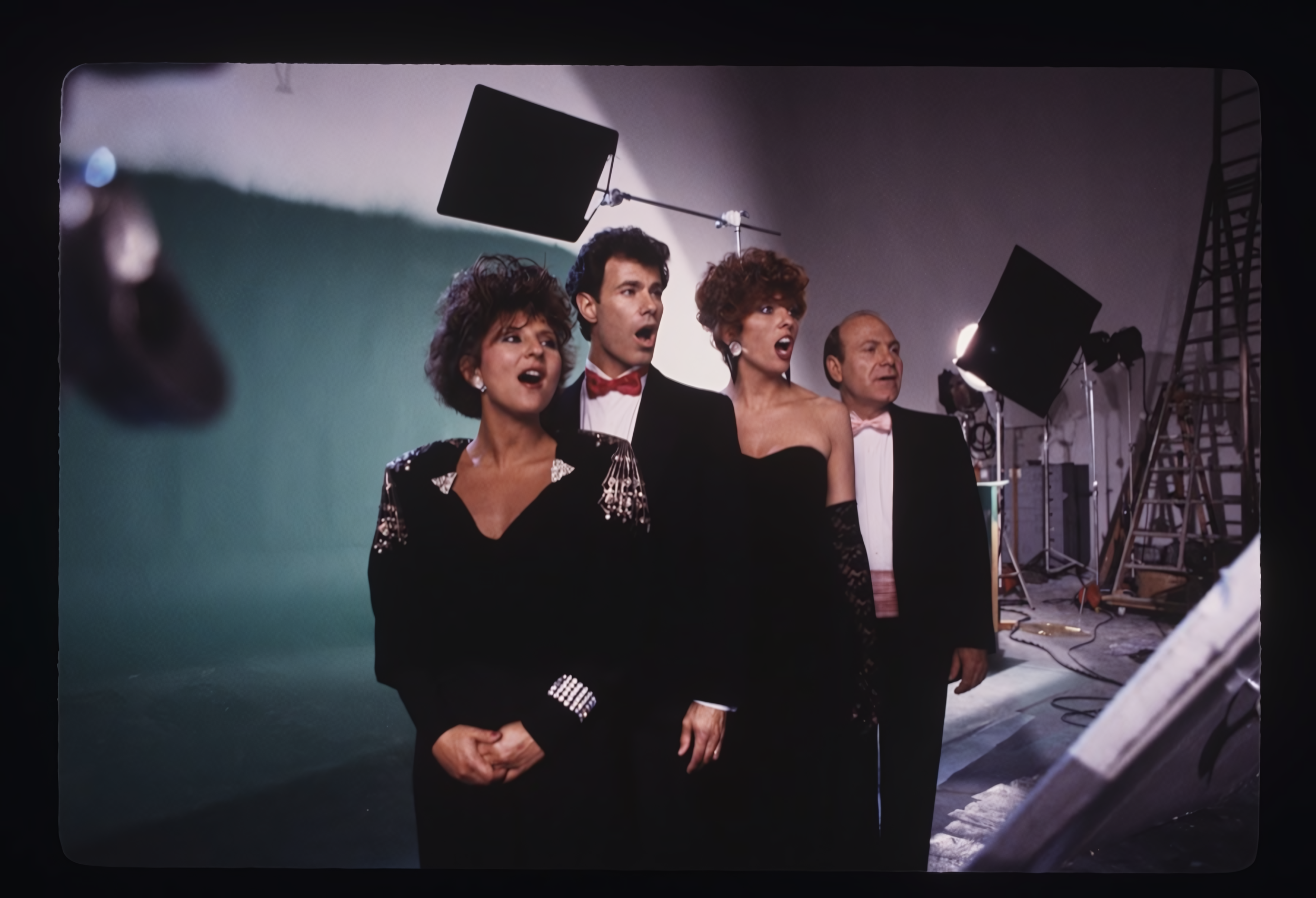 Filming crew on set with studio lights and equipment, standing in front of a green screen, wearing formal attire.