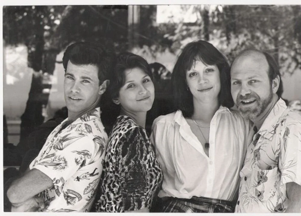 Four people standing outdoors, posing for a photo, with trees in the background.