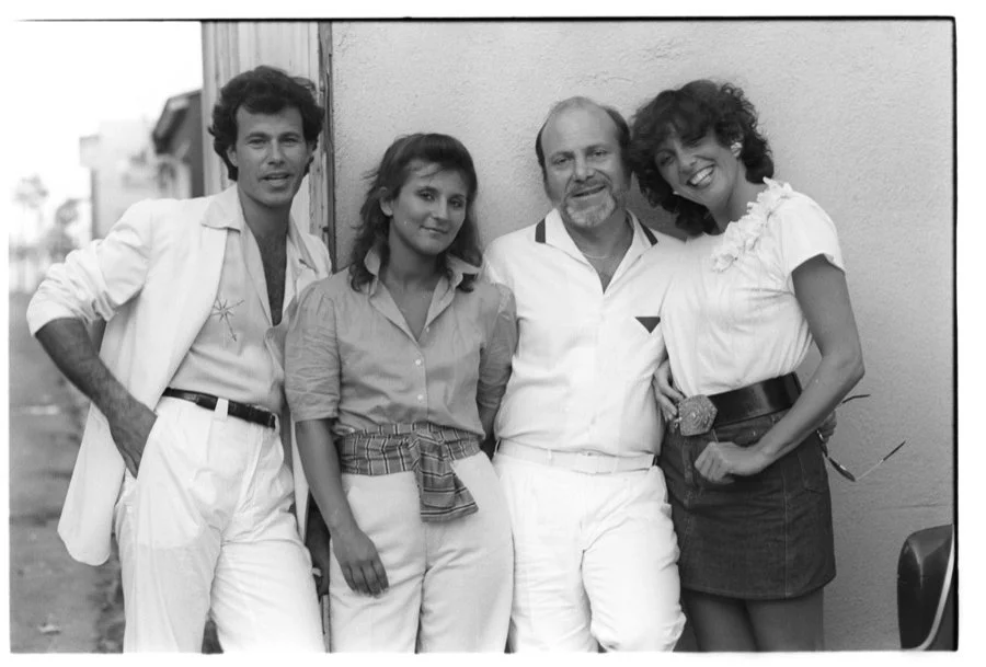 Four people standing together outdoors near a wall, smiling for the photo.
