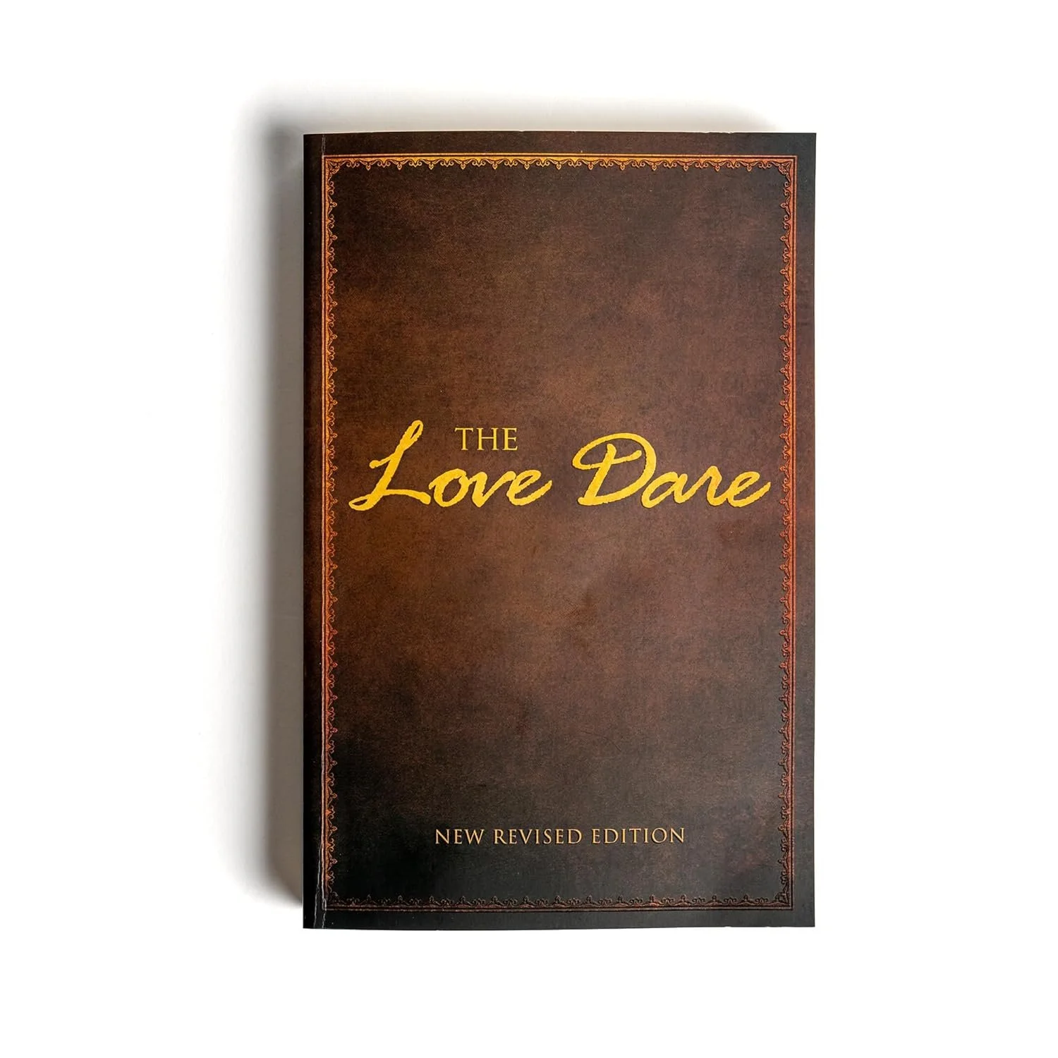 A book titled "The Love Dare" with a dark brown cover, decorative border, and gold lettering, labeled as a "New Revised Edition."