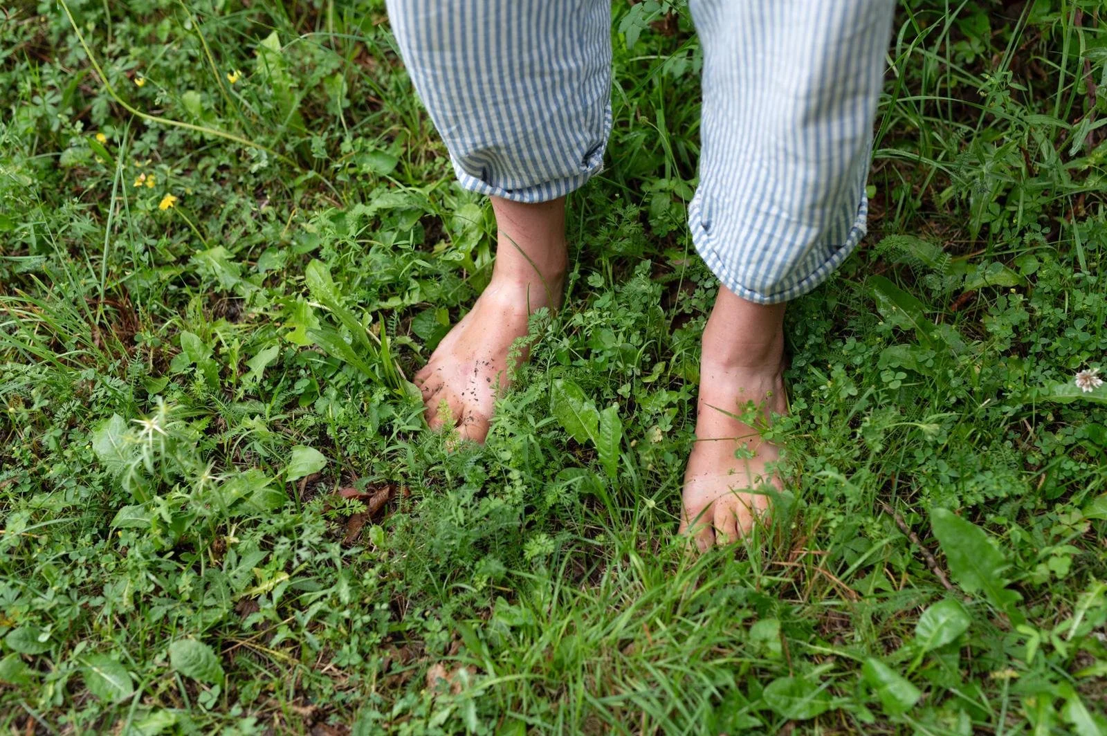 Bare feet standing on green grass with a person in striped pajama pants.