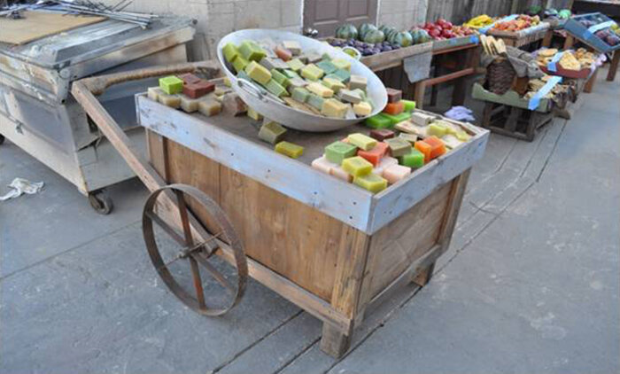 A wooden cart at an outdoor market displaying colorful soap bars on a table.