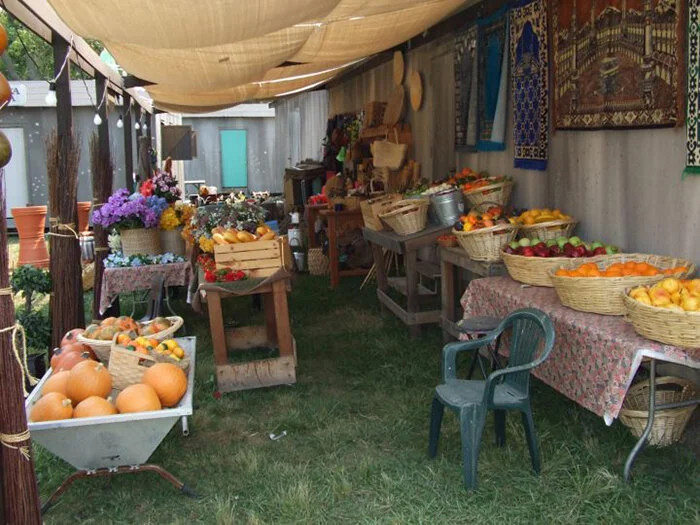 A fruit and flower stand at an outdoor market with various baskets of fruit, flowers, and decorative items on tables and on the ground under a canopy.