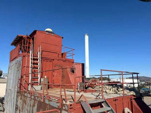 Close-up of an old red industrial structure with railings and stairs, against a clear blue sky.
