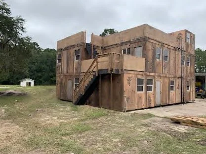 A two-story wooden building with an exterior staircase on a grassy area