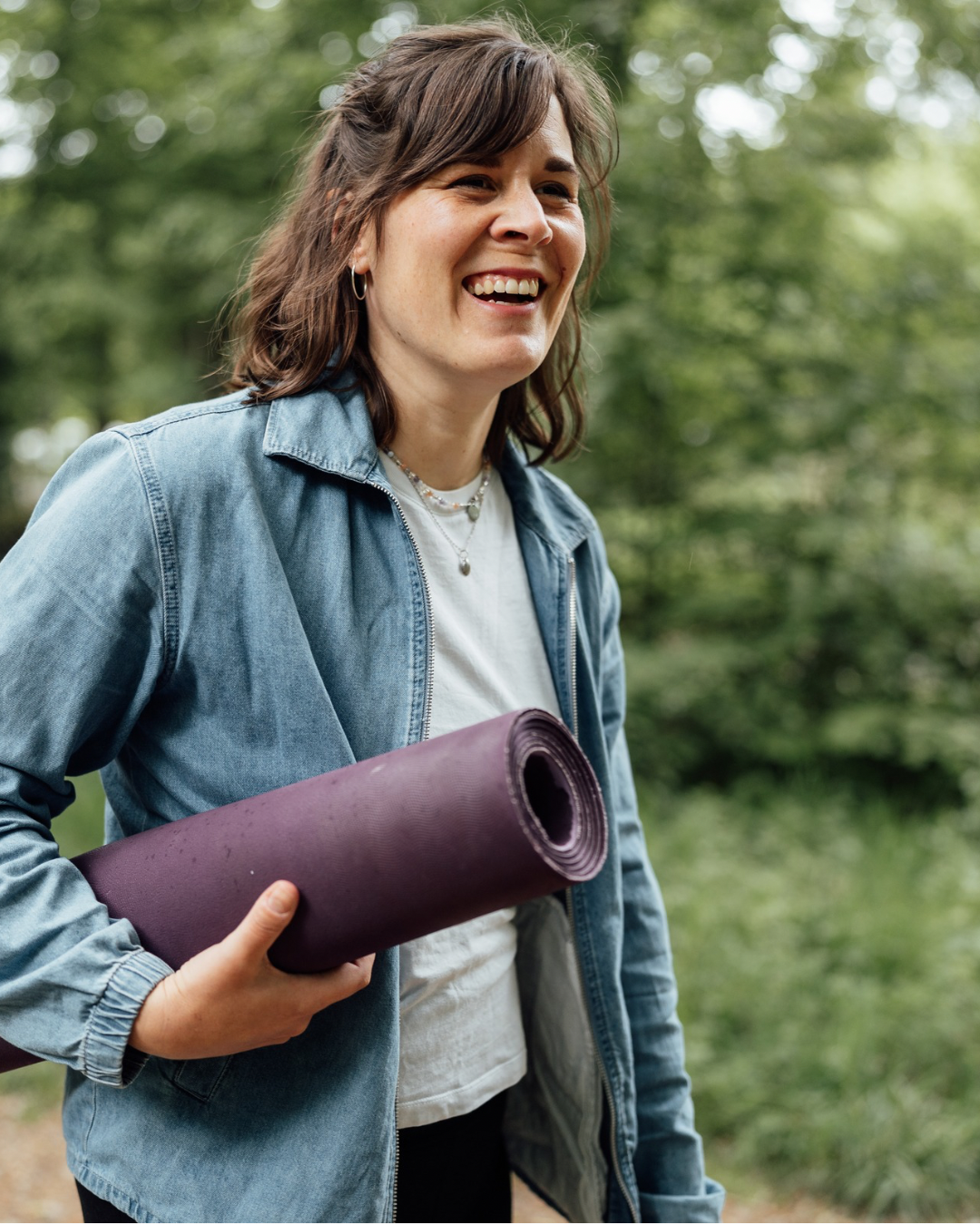 Lächelnde junge Frau mit Yogamatte in der Natur