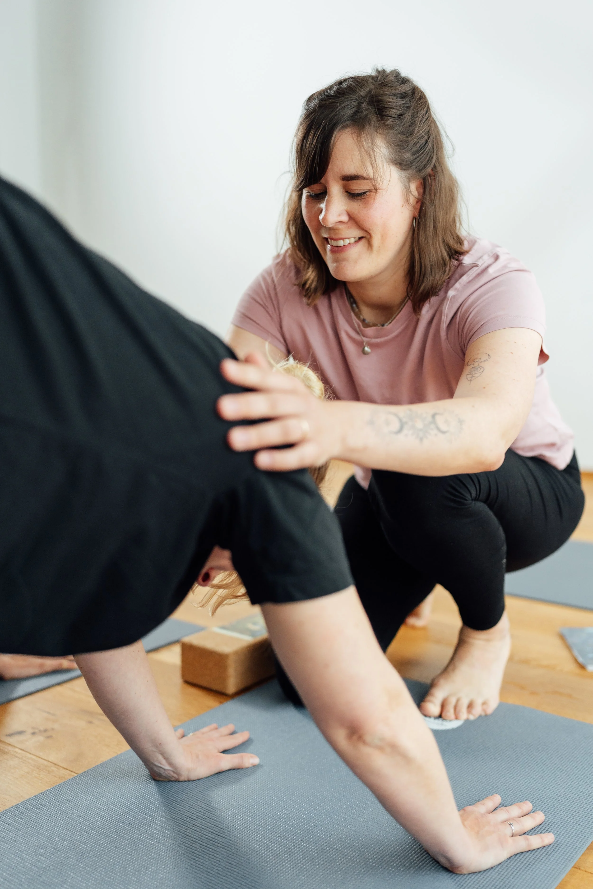 Zwei Frauen üben Yoga auf Yogamatten im Innenraum. Eine Frau trägt ein pinkes T-Shirt und die andere eine schwarze Kleidung.