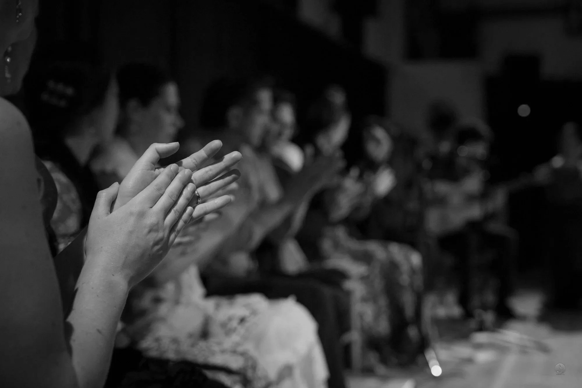 Close-up of hands clapping during a flamenco show, with people sitting in the background, in black and white.