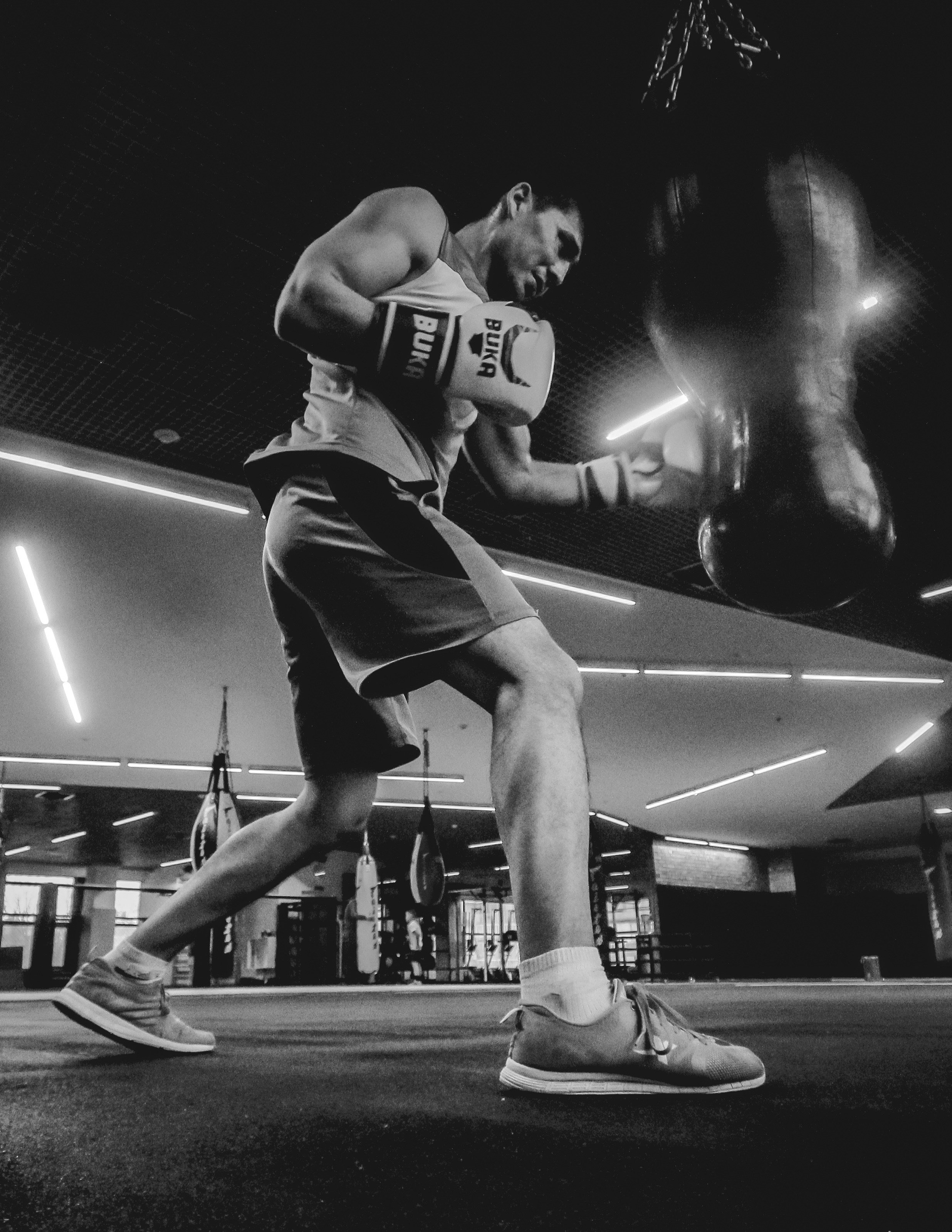 A man wearing boxing gloves and athletic clothing practices boxing at a gym with modern lighting.