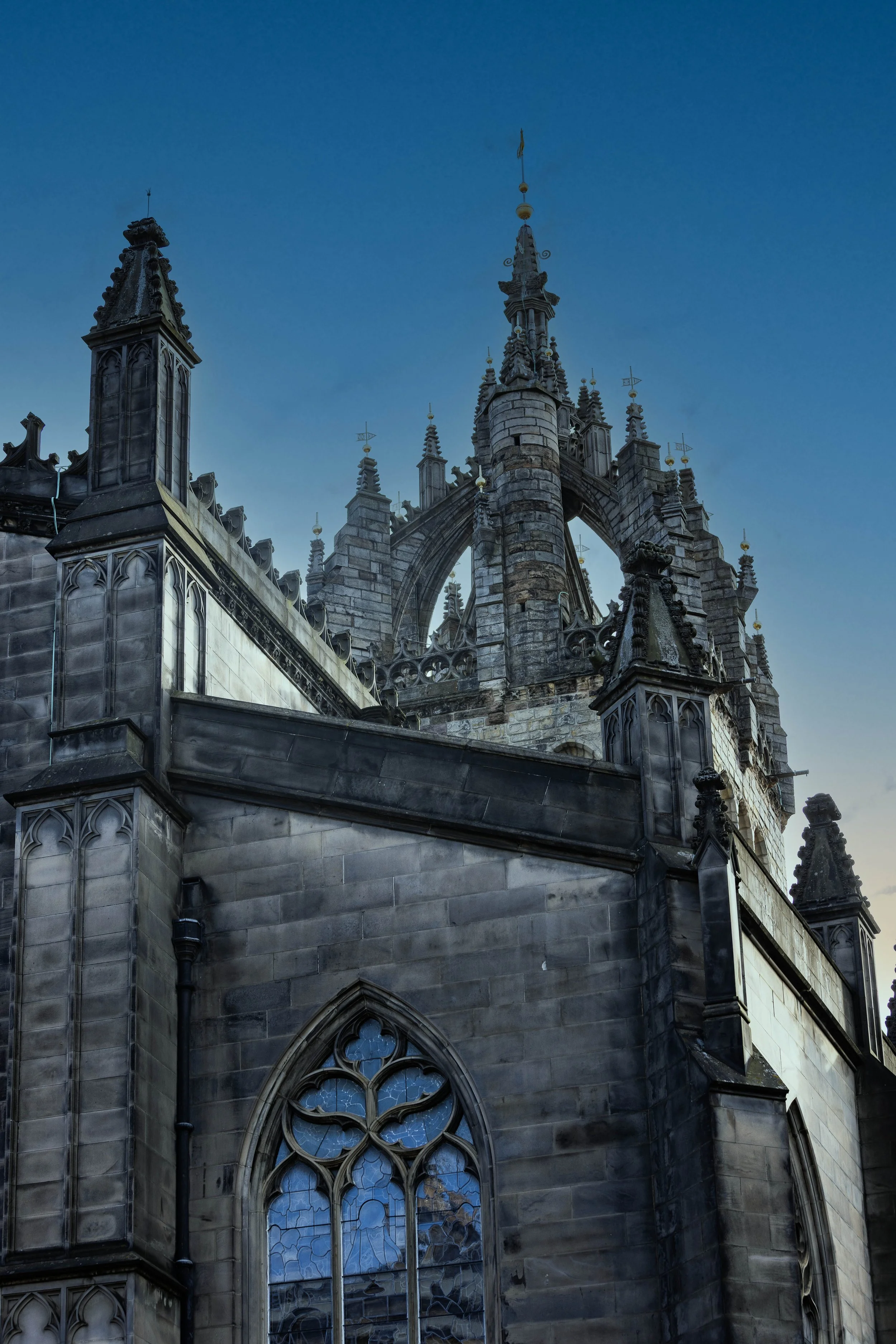 Close-up of a gothic cathedral's exterior showcasing intricate stone carvings, pointed arches, and stained-glass windows against a clear blue sky.