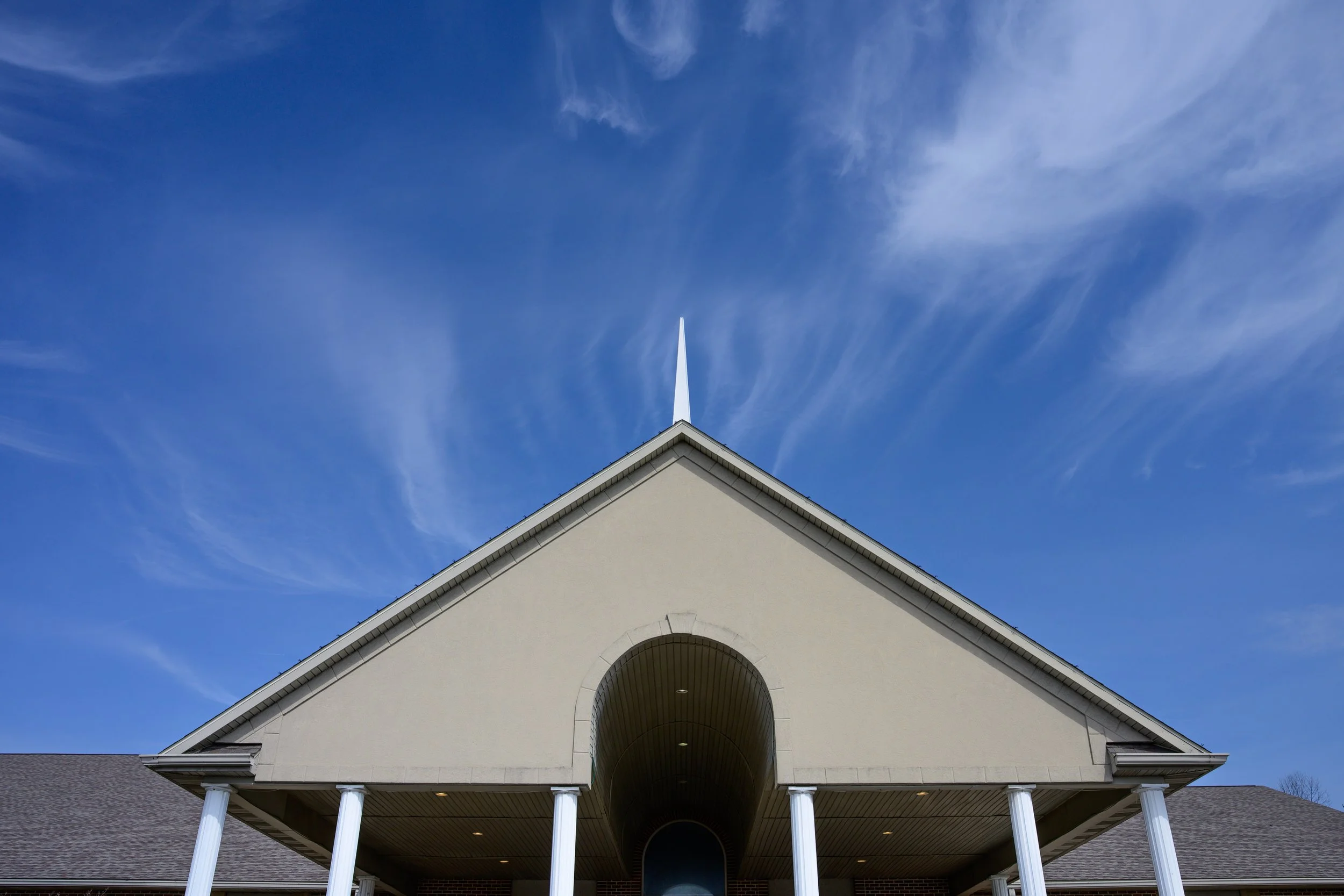 White church with a tall steeple against a blue sky with wispy clouds.