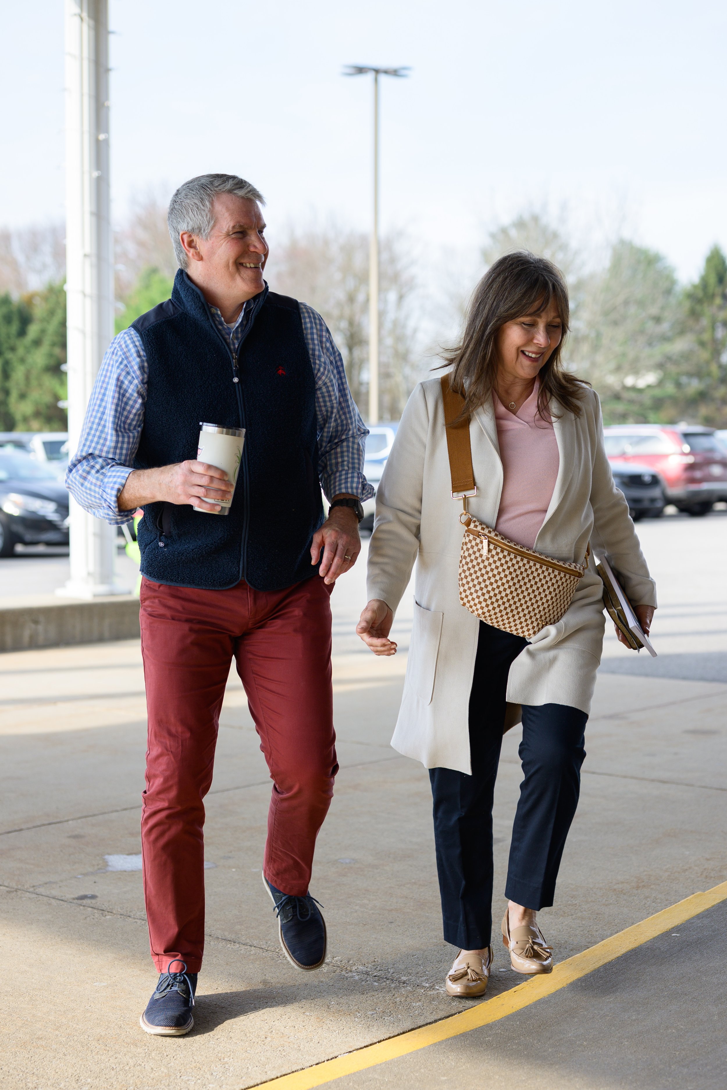 A man and woman walking and talking outdoors in a parking lot on a cloudy day.
