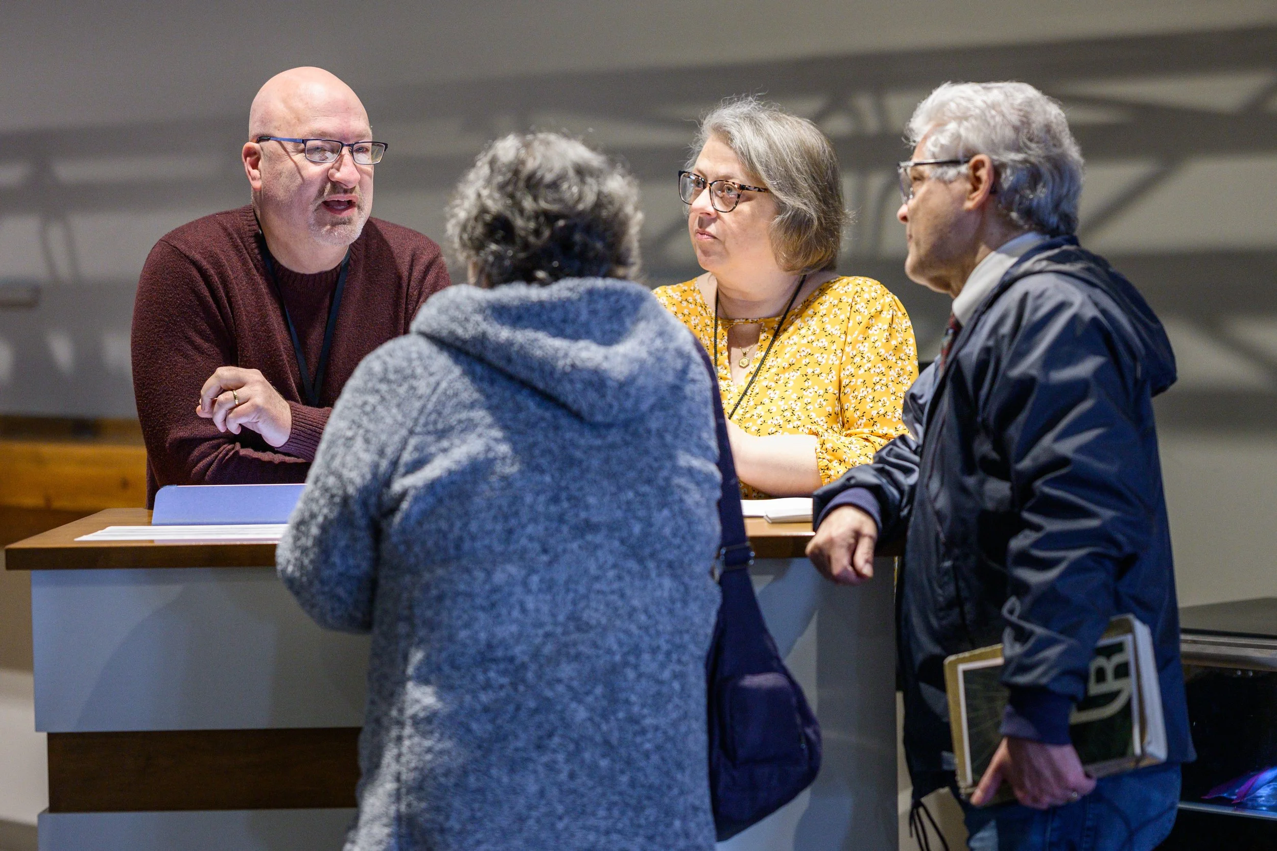 A group of four people engaged in a discussion at a table, with one man talking and three others listening, in an indoor setting.