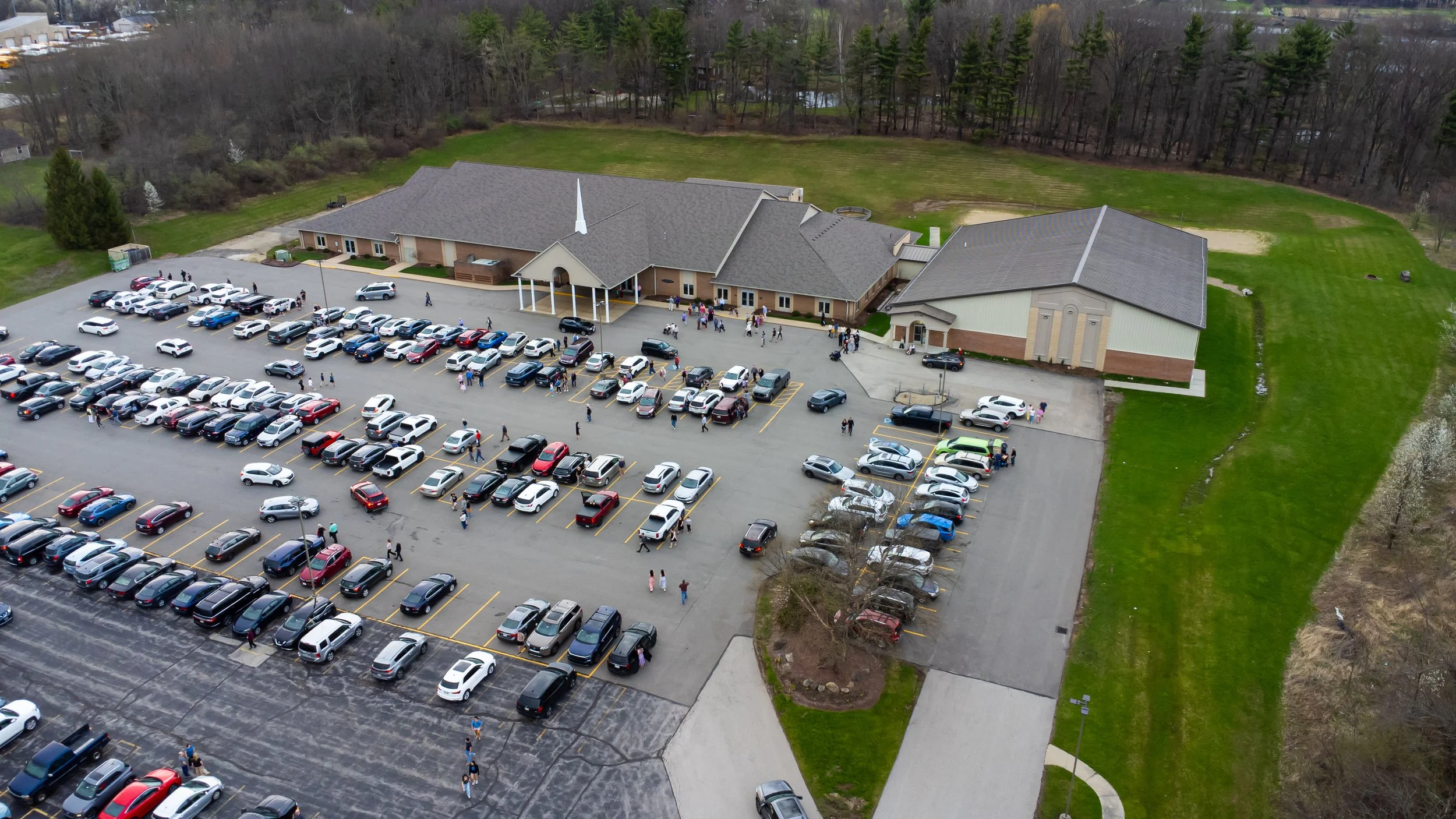 An aerial view of a church with a parking lot filled with cars and people walking around.