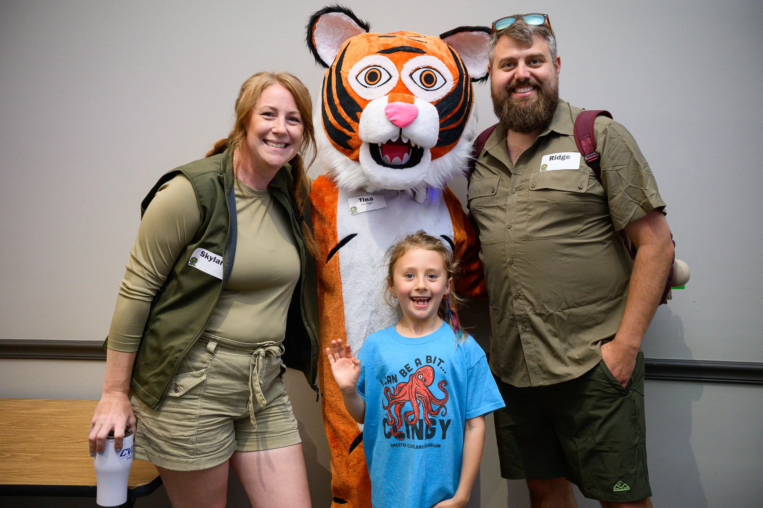Two adults and a child standing with a person in a tiger costume in front of a plain wall.